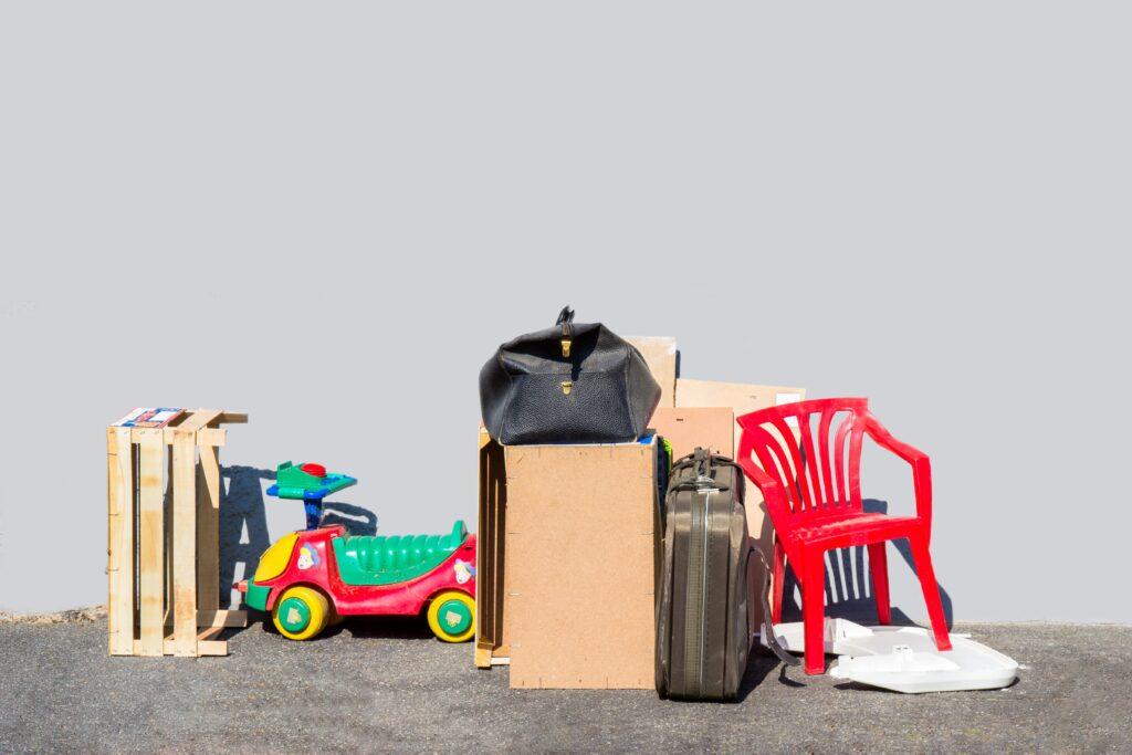 Verschiedene Gegenstände, darunter ein roter Plastikstuhl, ein Kinderauto, Kisten und eine Tasche, stehen zur Abholung auf einem Gehweg als Teil einer Entrümpelung in Essen.