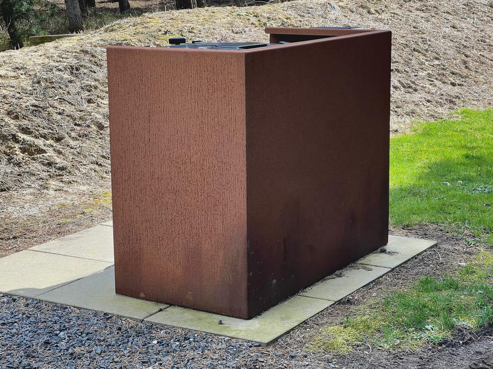 Rostfarbene Mülltonnenbox aus Metall im Garten, die für ein sauberes und organisiertes Erscheinungsbild sorgt