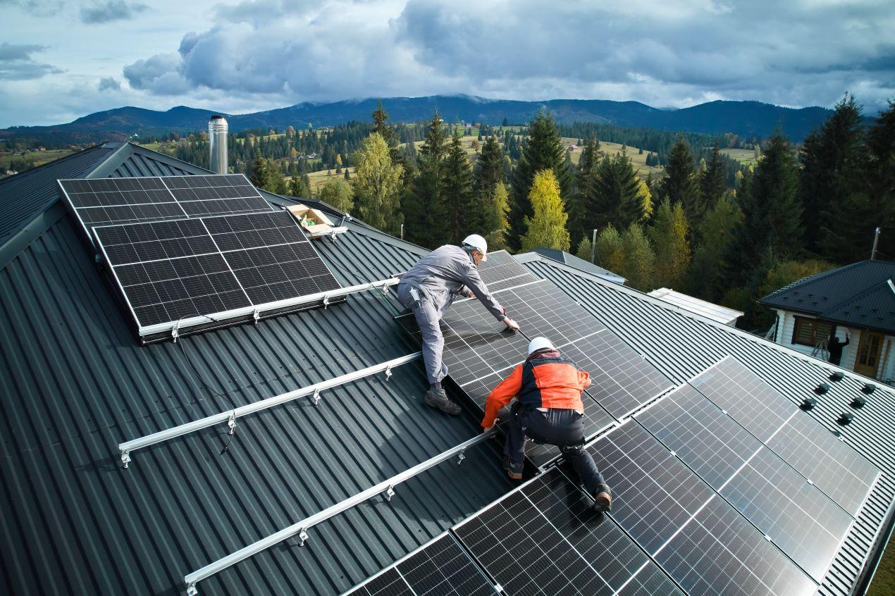 Zwei Installateure montieren Solarmodule auf einem Metallwellendach, im Hintergrund eine ländliche Landschaft – Installation einer Photovoltaikanlage in Gera.